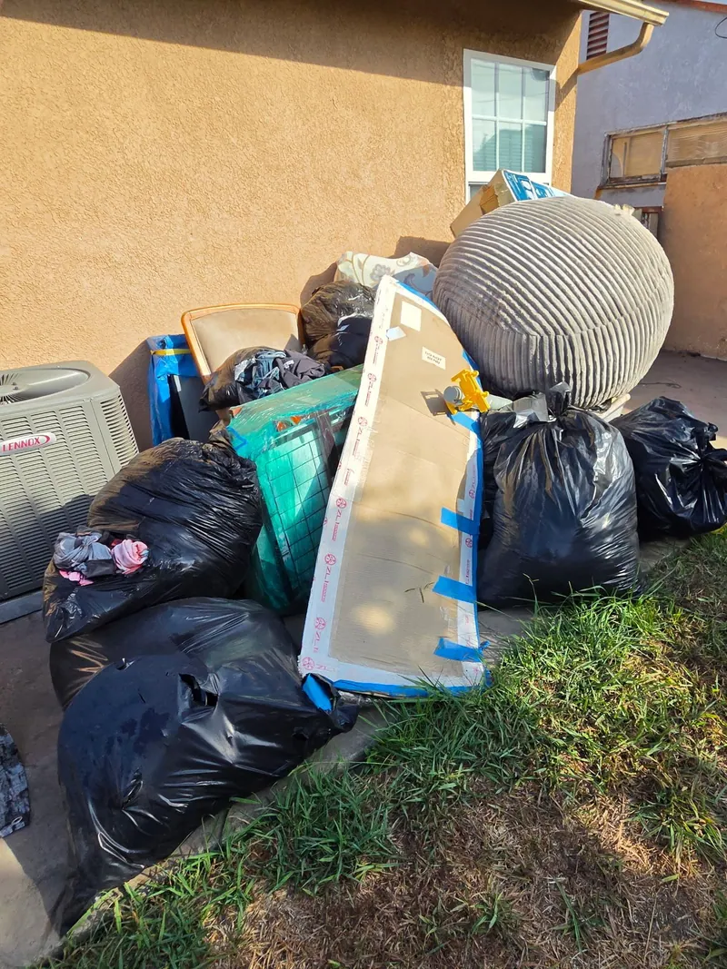 Bagged household junk, a bean bag and an old chair piled on a back patio for pickup
